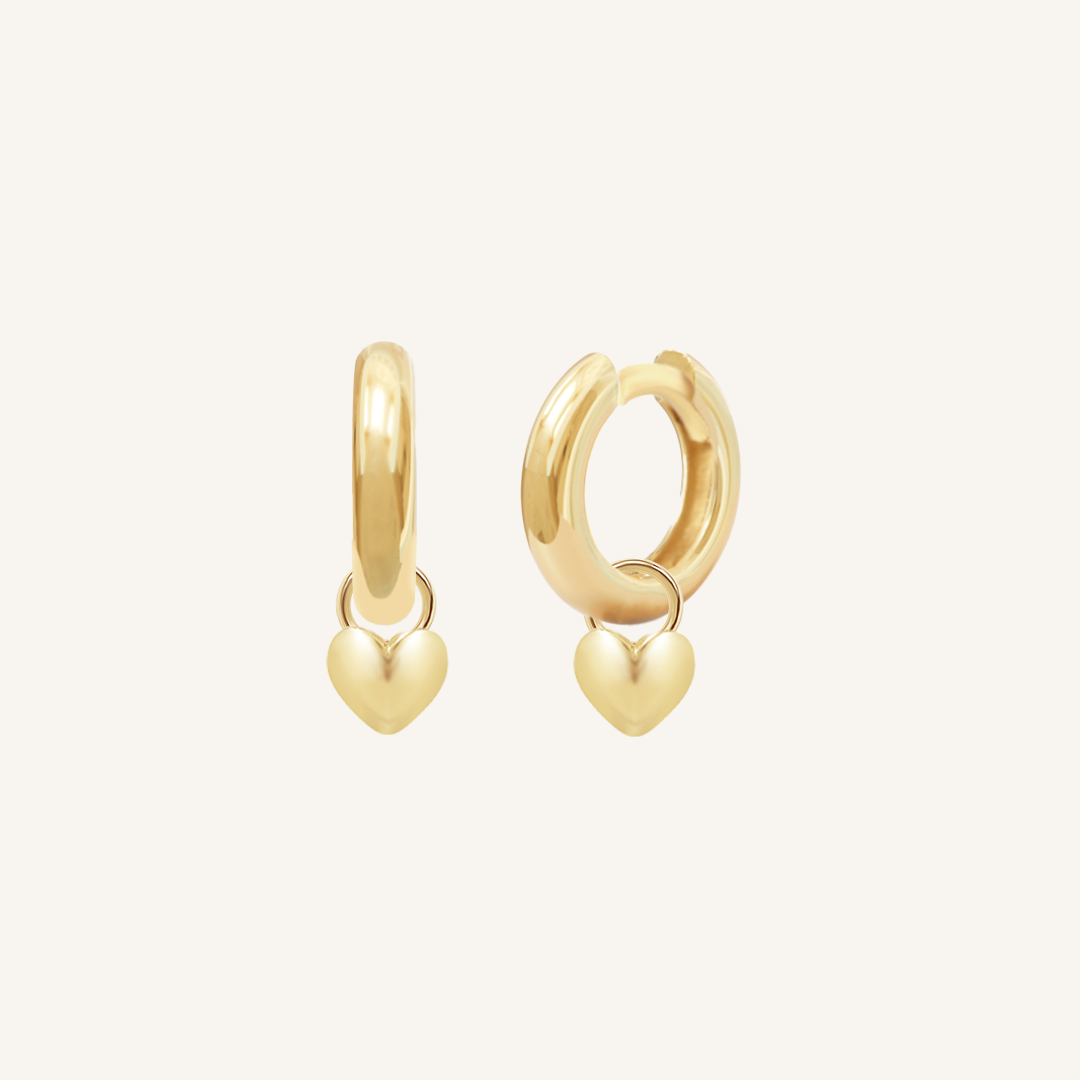 A pair of gold-colored hoop earrings with a dangling heart charm.