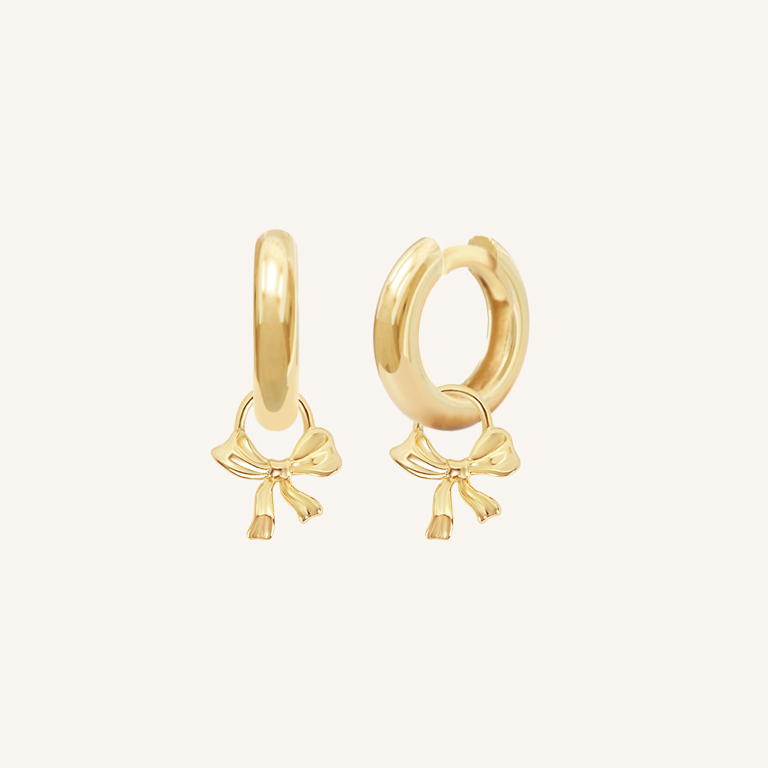 A pair of gold-tone hoop earrings with charm bows attached to them.