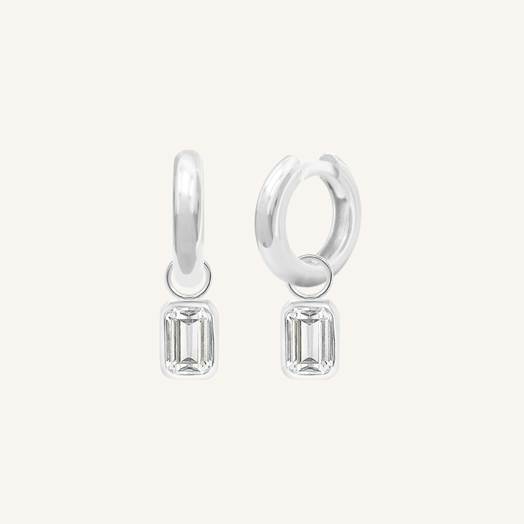 A pair of silver-colored hoop earrings with transparent crystal embellishments.
