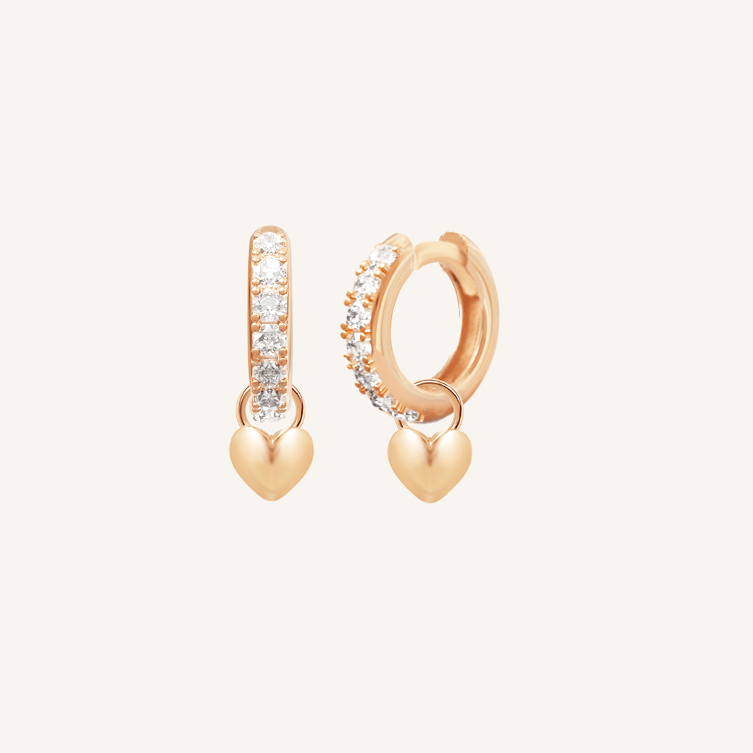 A pair of rose hoop earrings with cubic zirconias with heart charms attached to them, displayed against a white background.