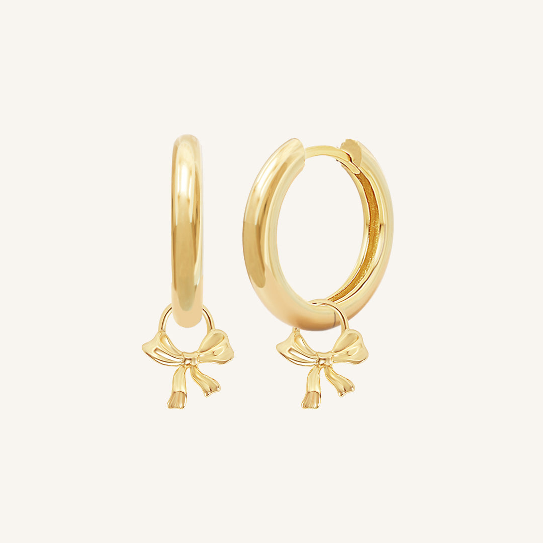 A pair of gold-colored hoop earrings with charm pendants attached to them, displayed against a white background.