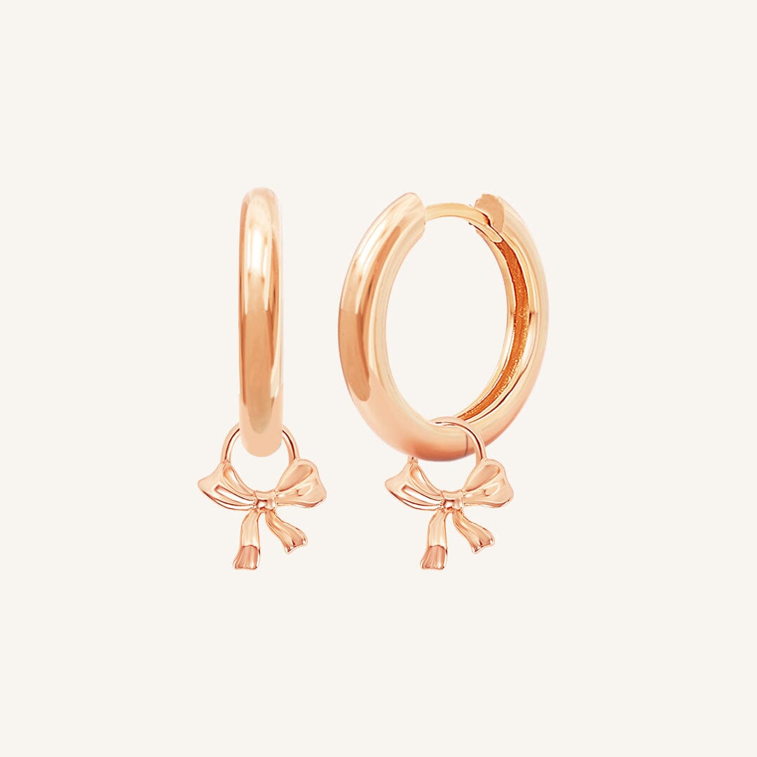 A pair of rose-colored hoop earrings with charm pendants attached to them, displayed against a white background.