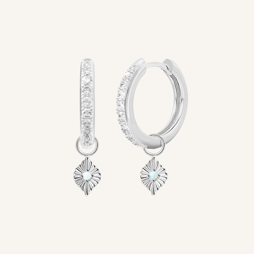 A pair of silver hoop earrings with cubic zirconia and diamond shaped hoop charms featuring a faux opal
