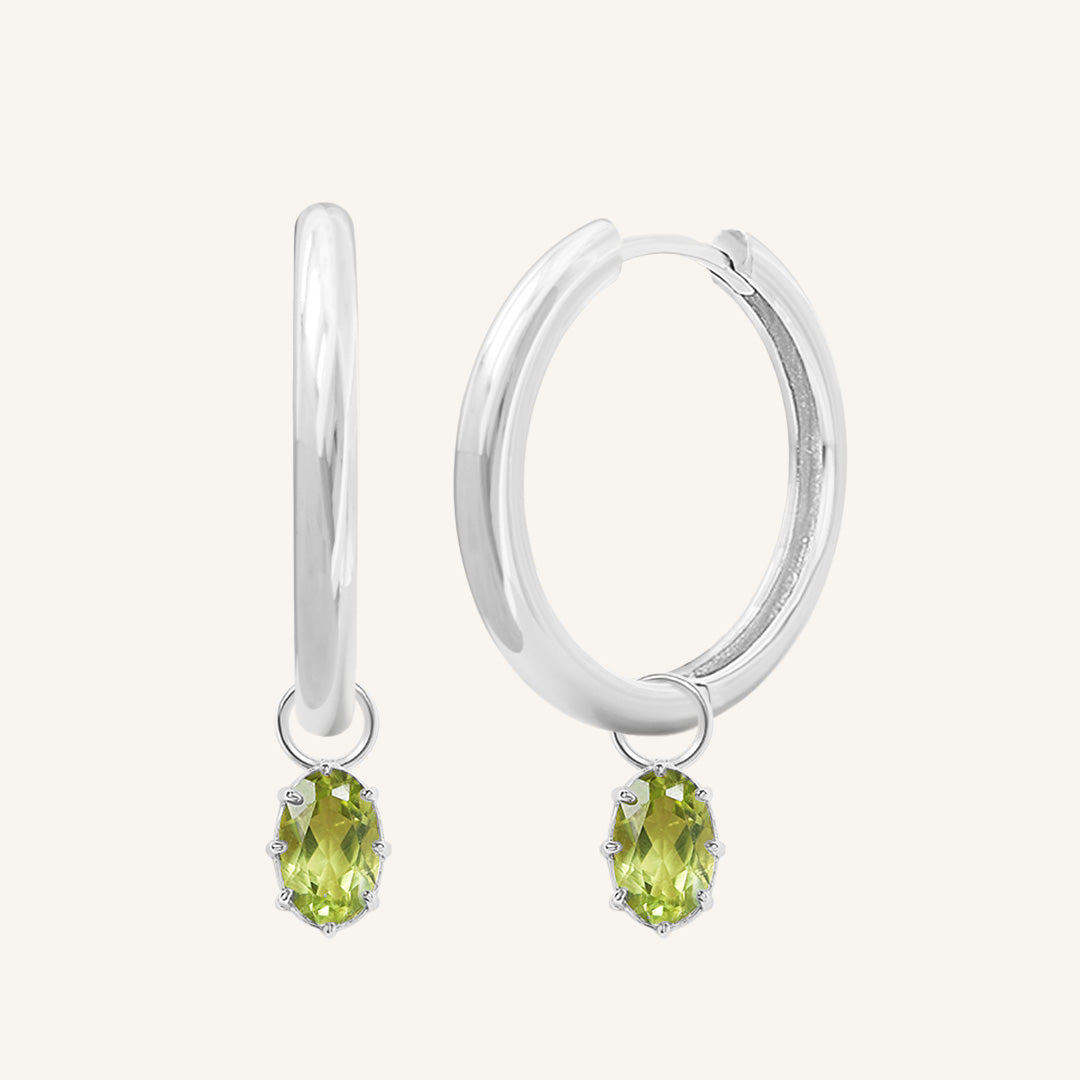 A pair of silver-tone hoop earrings with olive green charms attached to them.