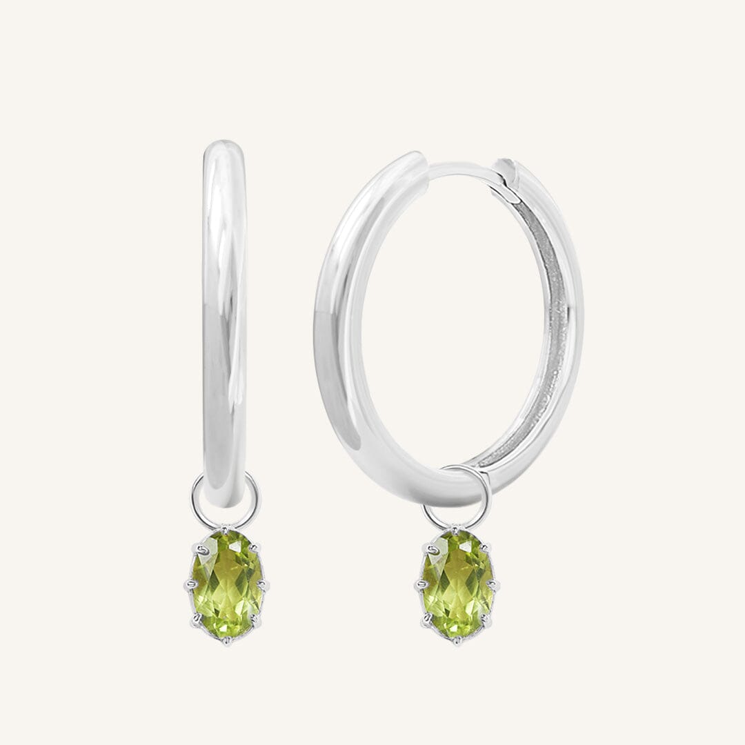 A pair of silver-tone hoop earrings with olive green charms attached to them.