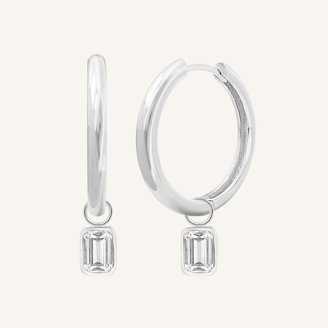 A pair of silver-colored hoop earrings with transparent crystal embellishments.