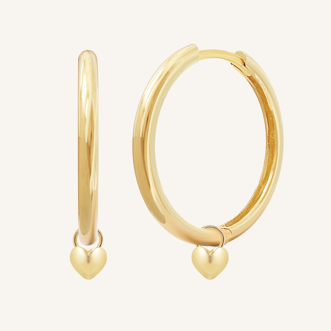A pair of gold-colored hoop earrings with a dangling heart charm.