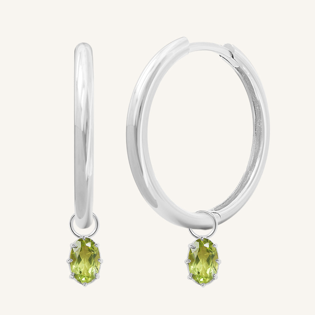 A pair of silver-tone hoop earrings with olive green charms attached to them.