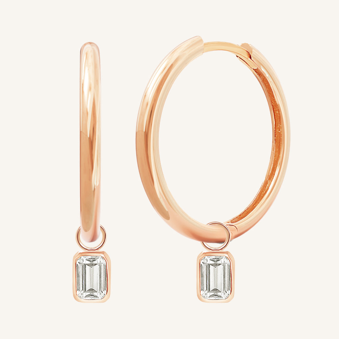 A pair of rose-colored hoop earrings with transparent crystal embellishments.