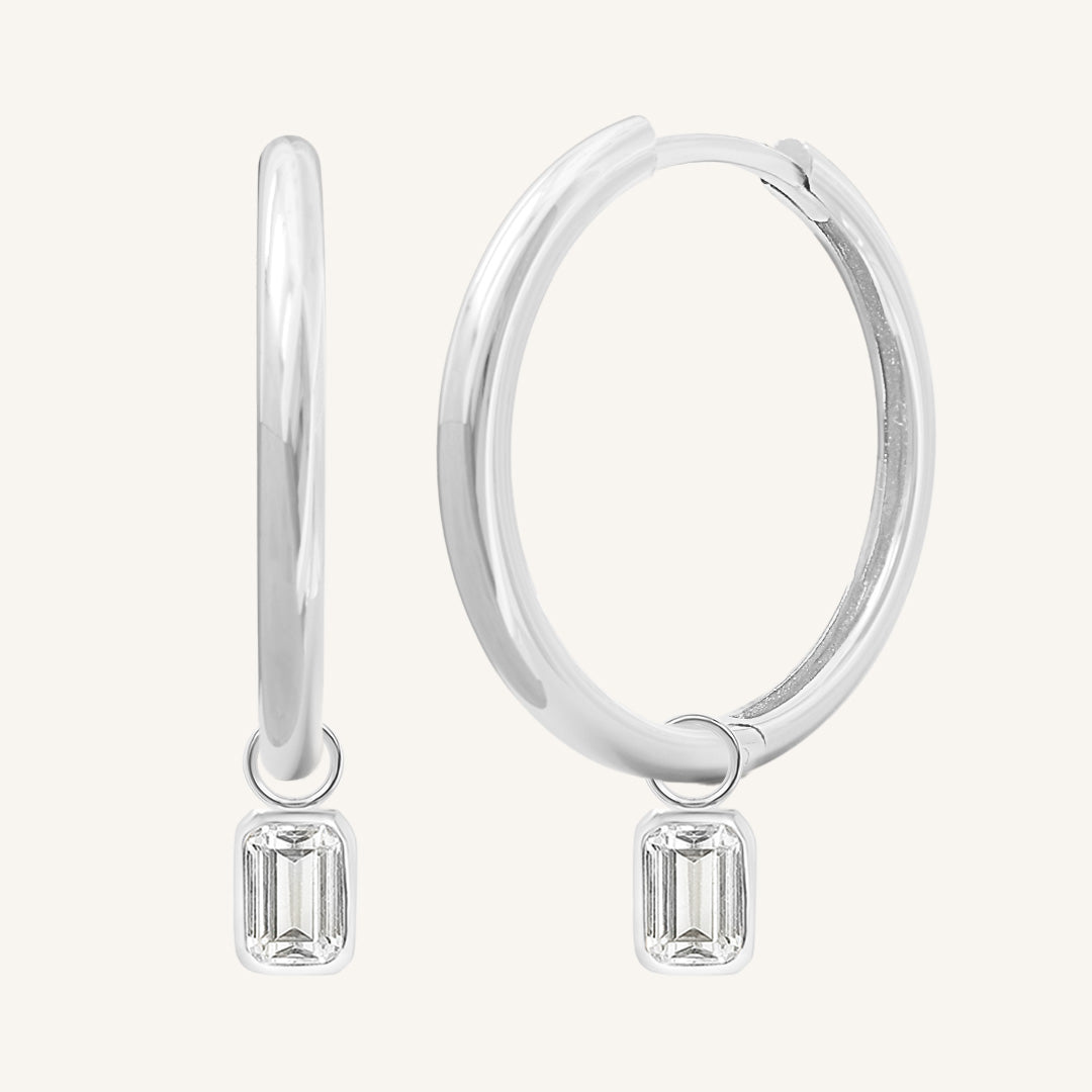A pair of silver-colored hoop earrings with transparent crystal embellishments.