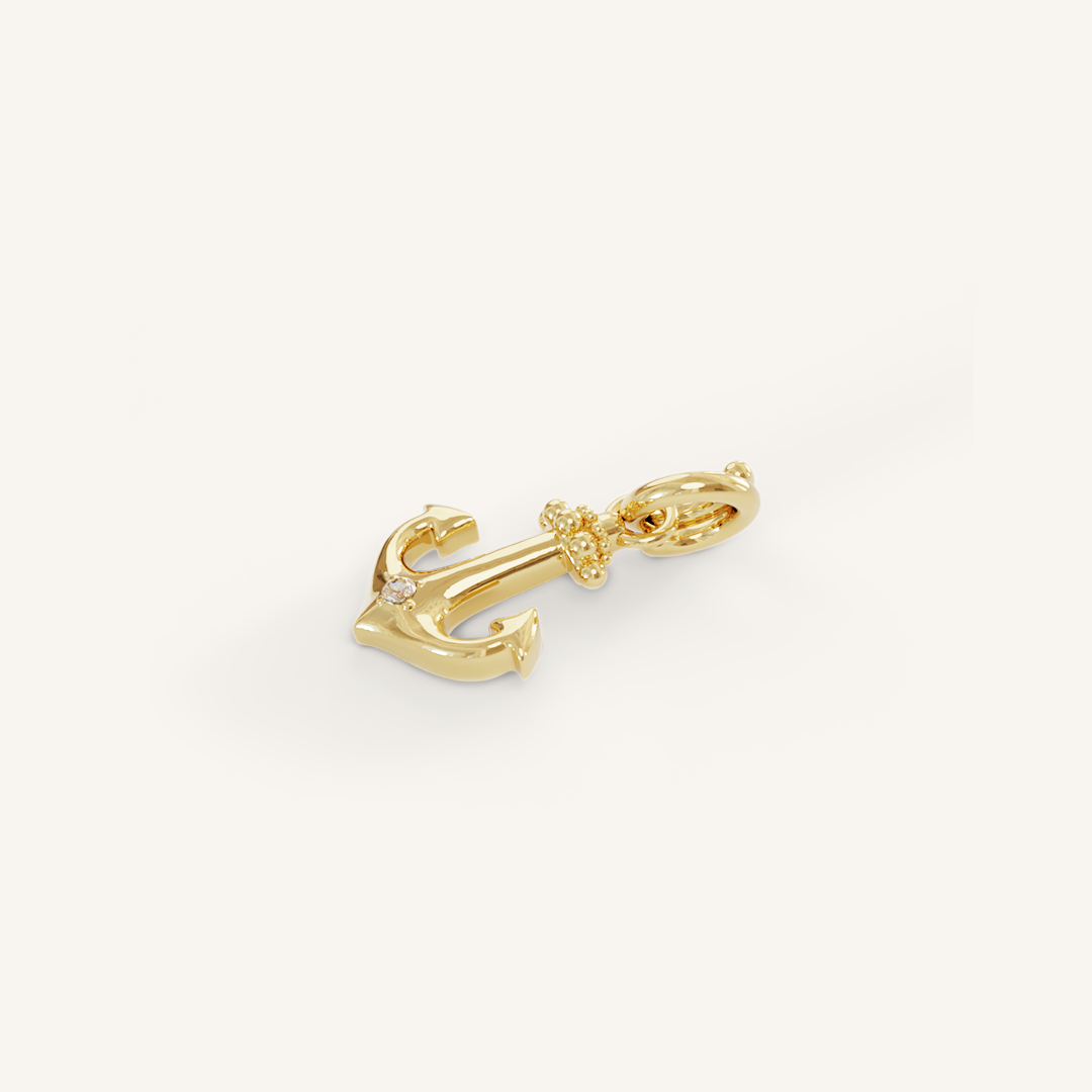 A gold anchor charm with a white cubic zirconia