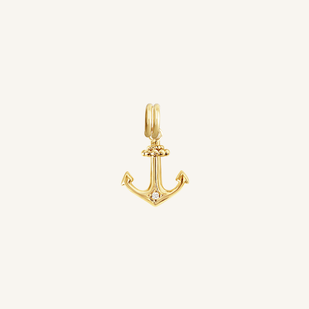 A gold anchor charm with a white cubic zirconia