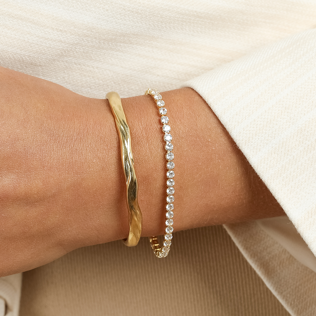 A gold-coloured tennis bracelet with clear cubic zirconias linked together, featuring a extender chain for adjustable length, worn on wrist.