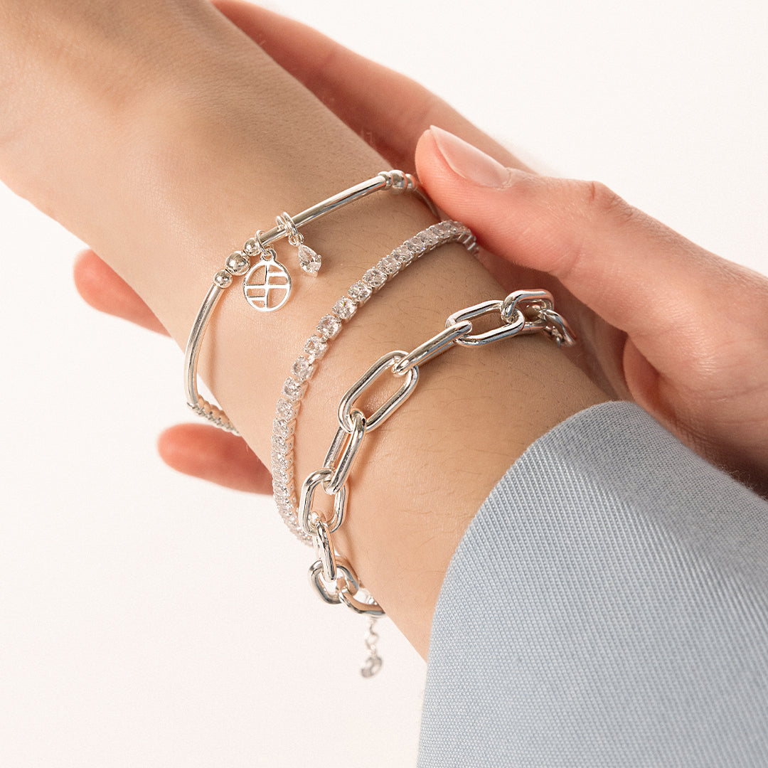 A silver-coloured tennis bracelet with clear cubic zirconias linked together, featuring a extender chain for adjustable length, on wrist.