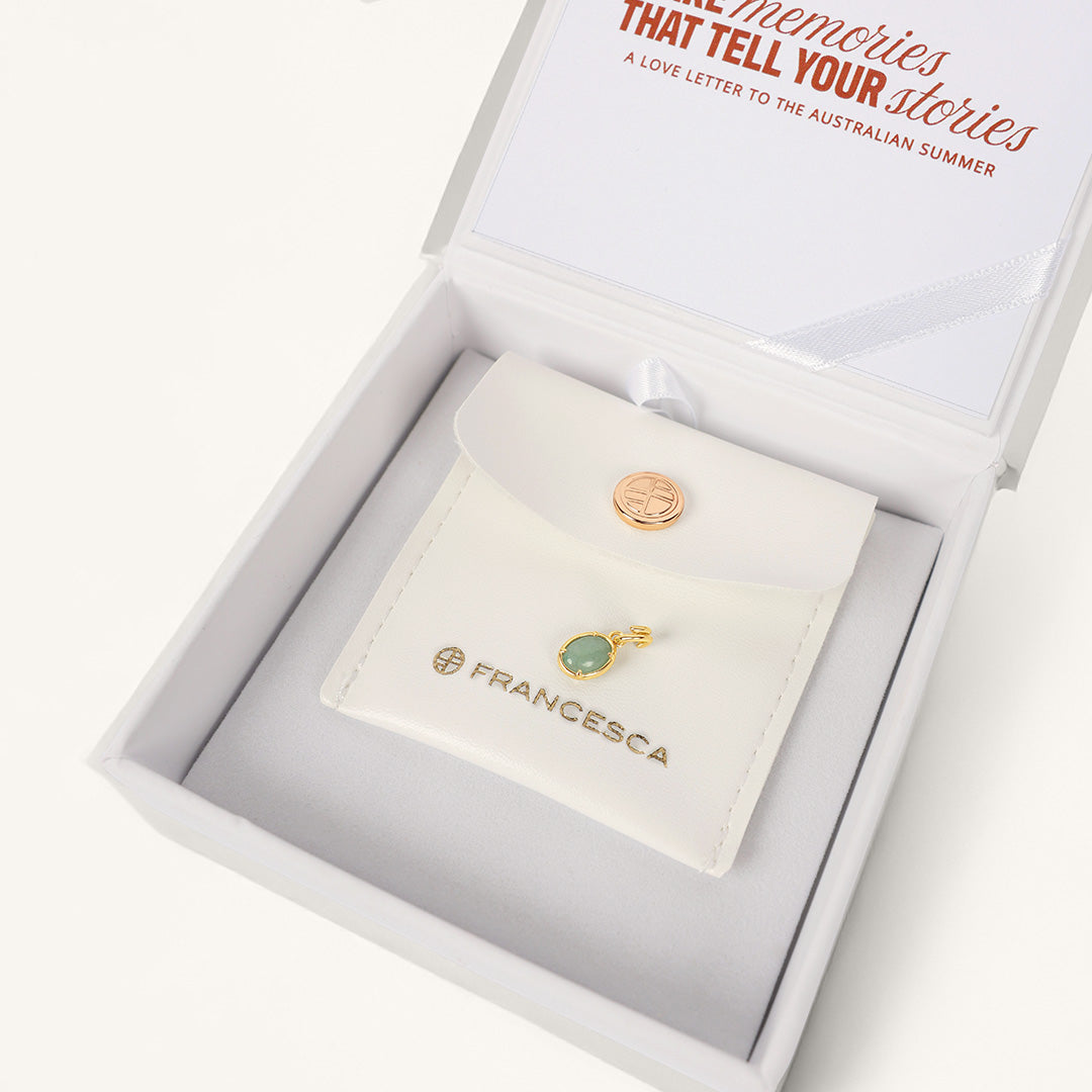 Gold pendant with a green stone, displayed in white box
