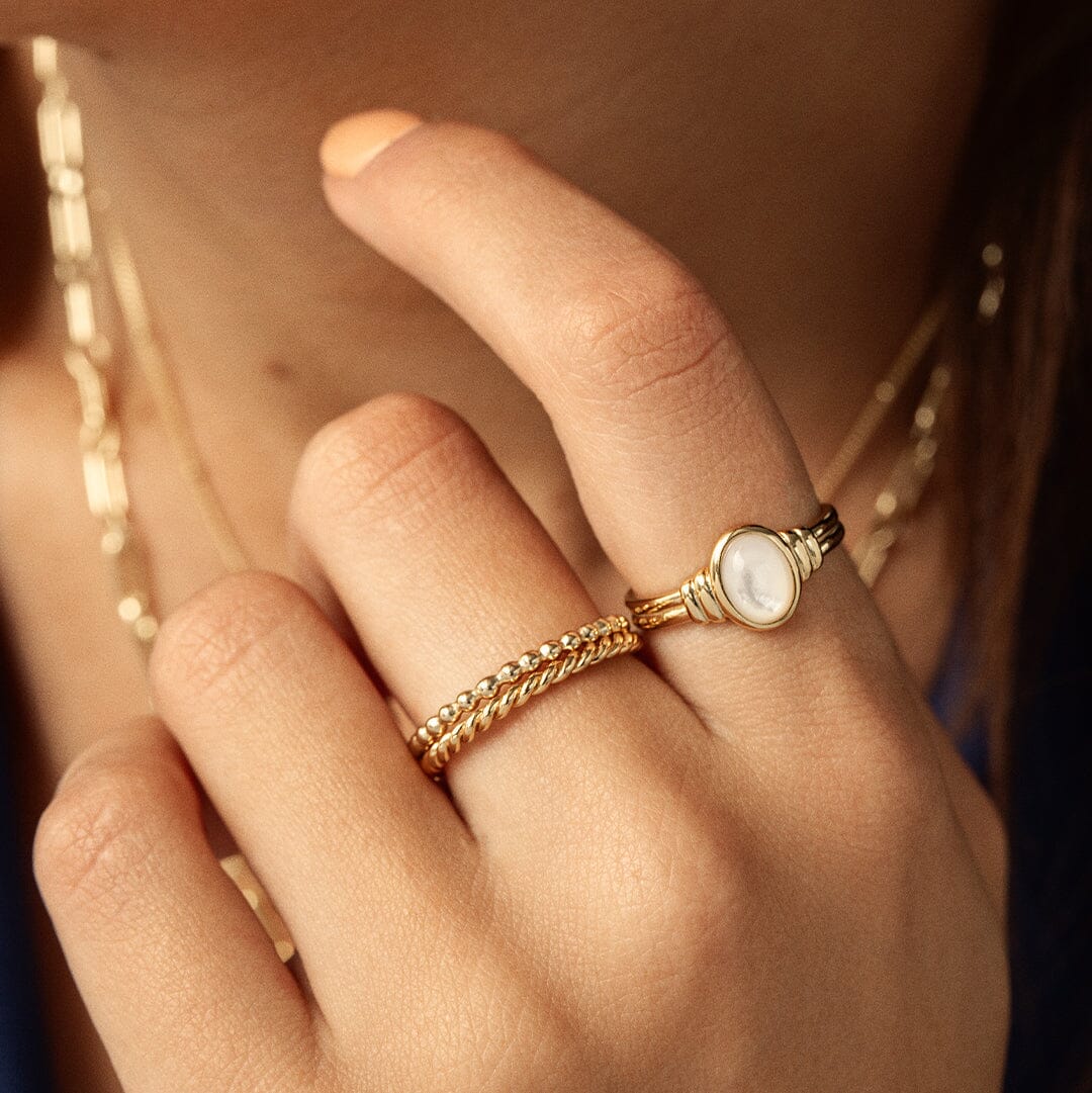 A gold coloured stacking ring with a simple, elegant design featuring small, uniform beads around its circumference close up worn on the finger