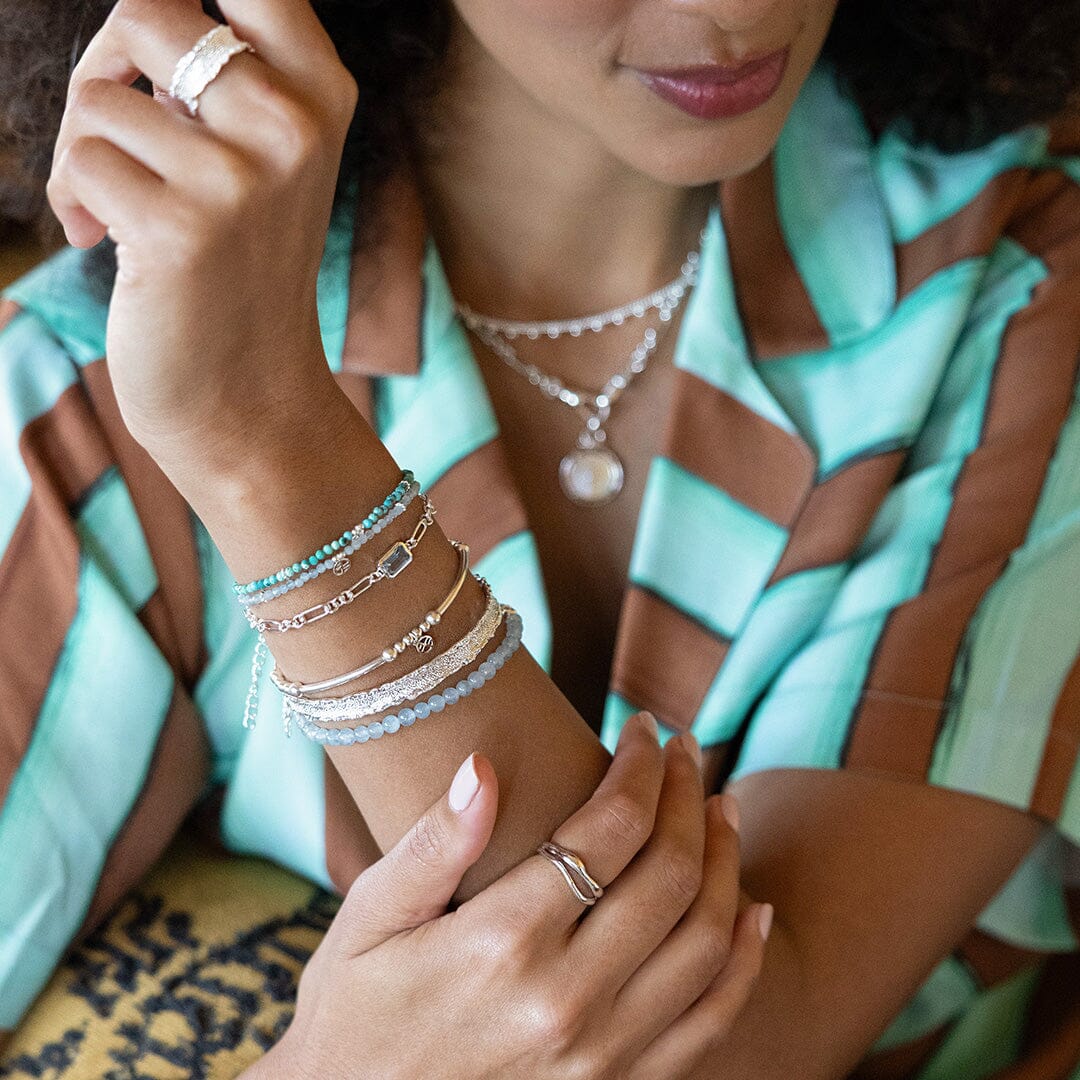 Close-up of a person's wrist with multiple bracelets and rings, wearing a patterned garment.