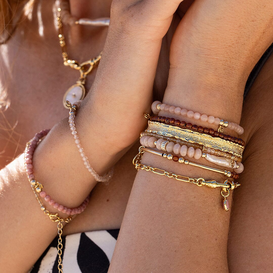 Close-up of a person's wrist wearing multiple gold and beaded bracelets.