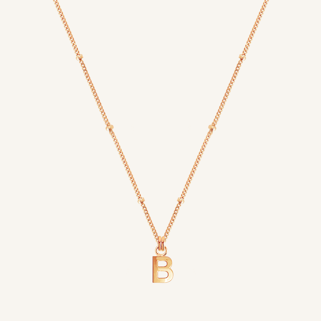 Rose gold necklace with a 'B' pendant on a light beige background