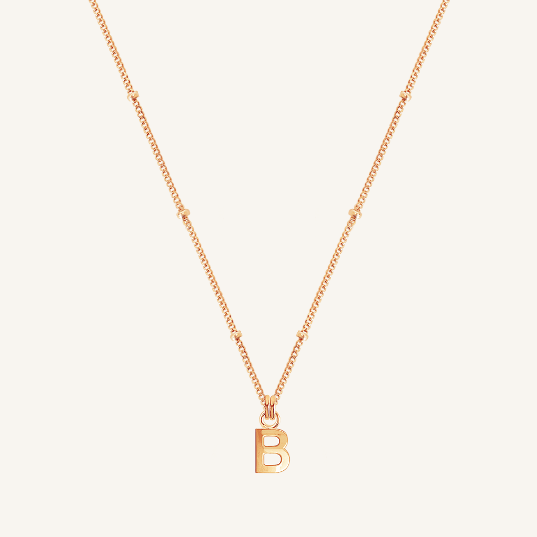 Rose gold necklace with a 'B' pendant on a light beige background