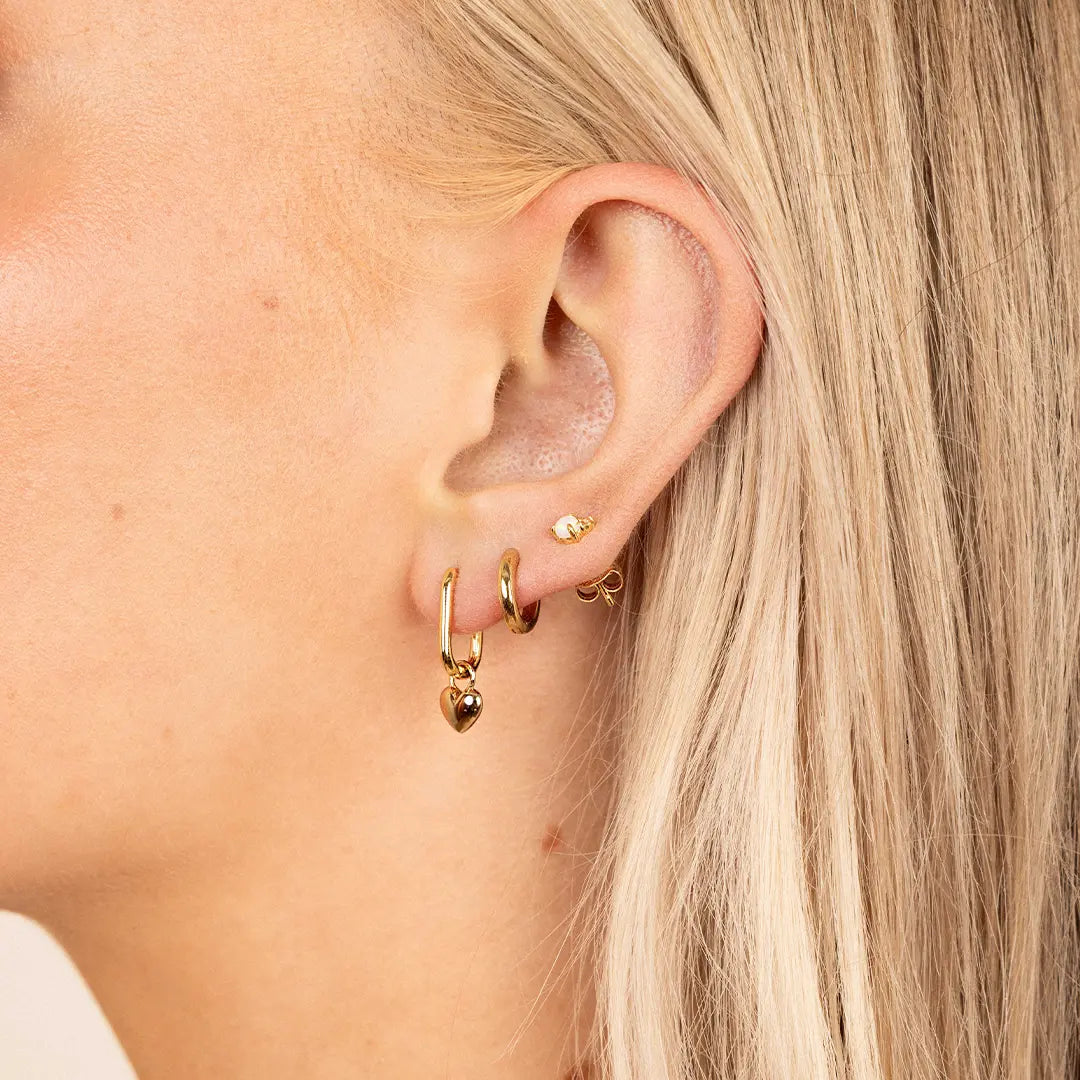 A pair of heart-shaped gold hoop charms, worn by model