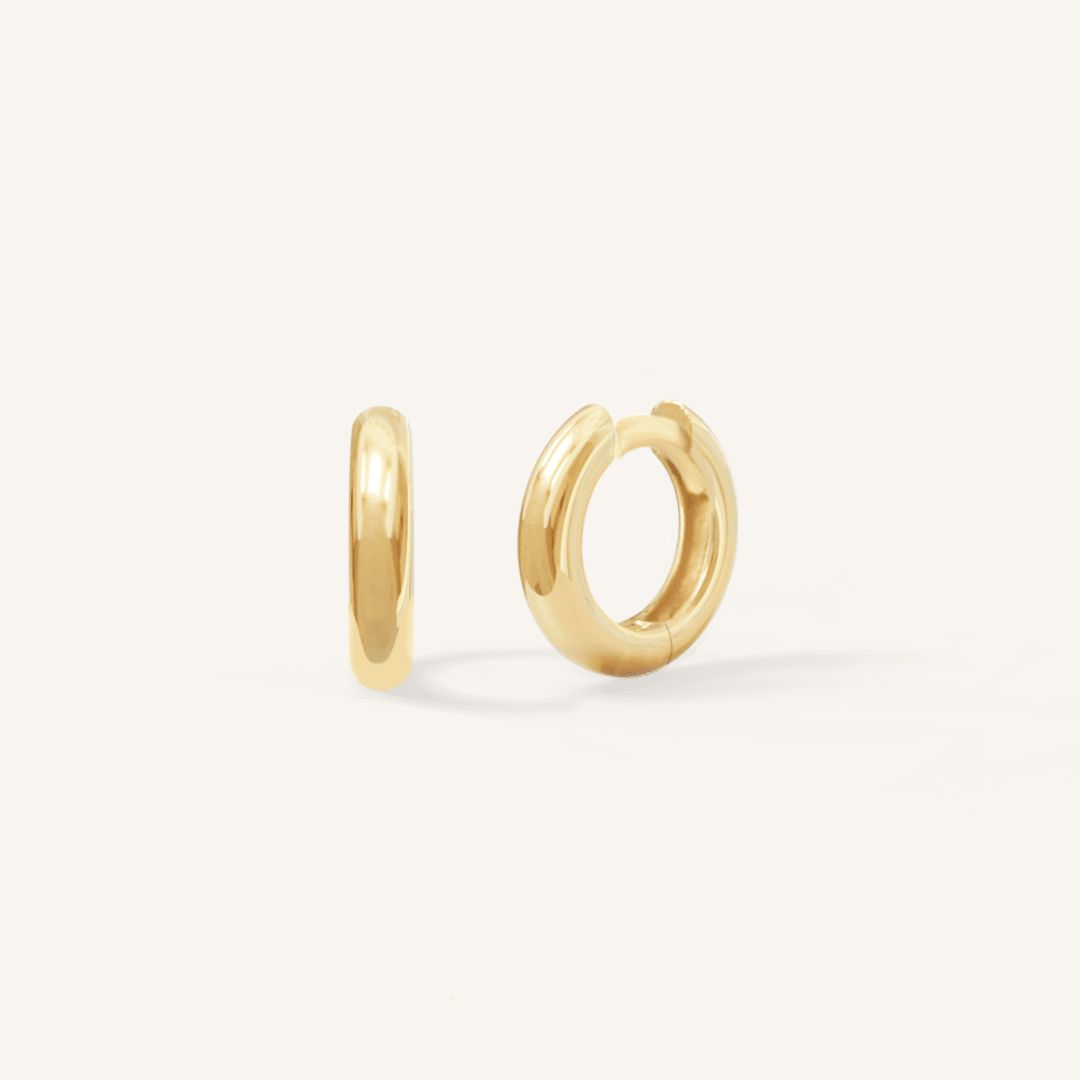 A pair of gold-colored huggie hoop earrings on a white background.