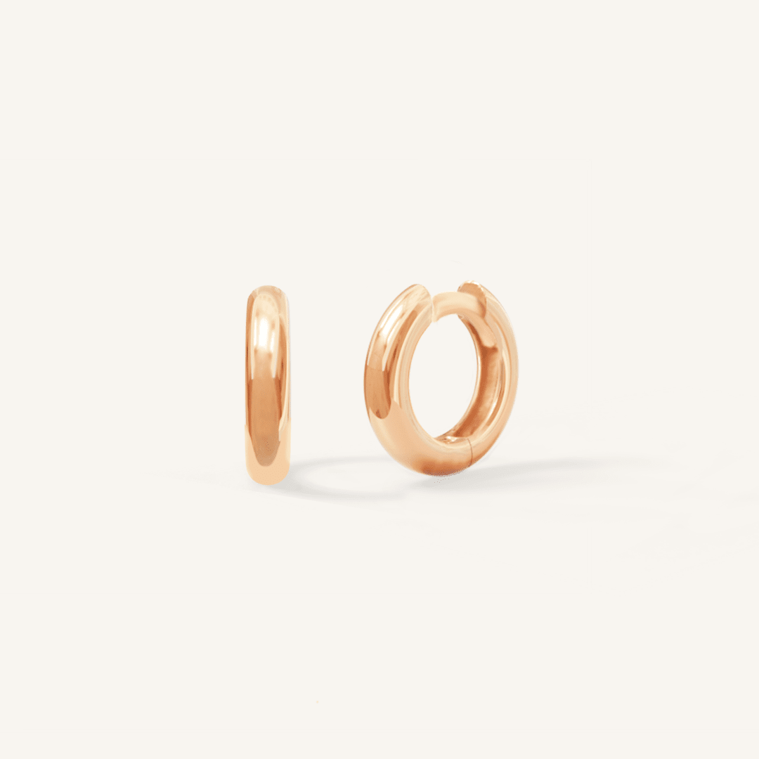 A pair of rose-colored huggie hoop earrings on a white background.