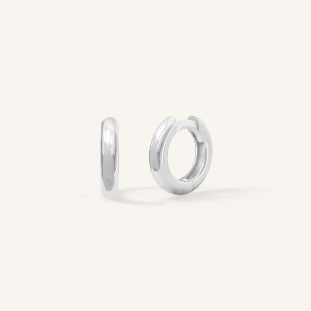 A pair of silver-colored huggie hoop earrings on a white background.