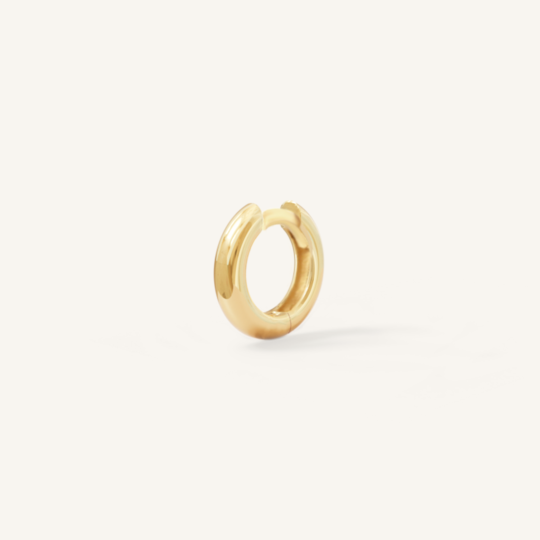 A gold huggie hoop earring on a white background.