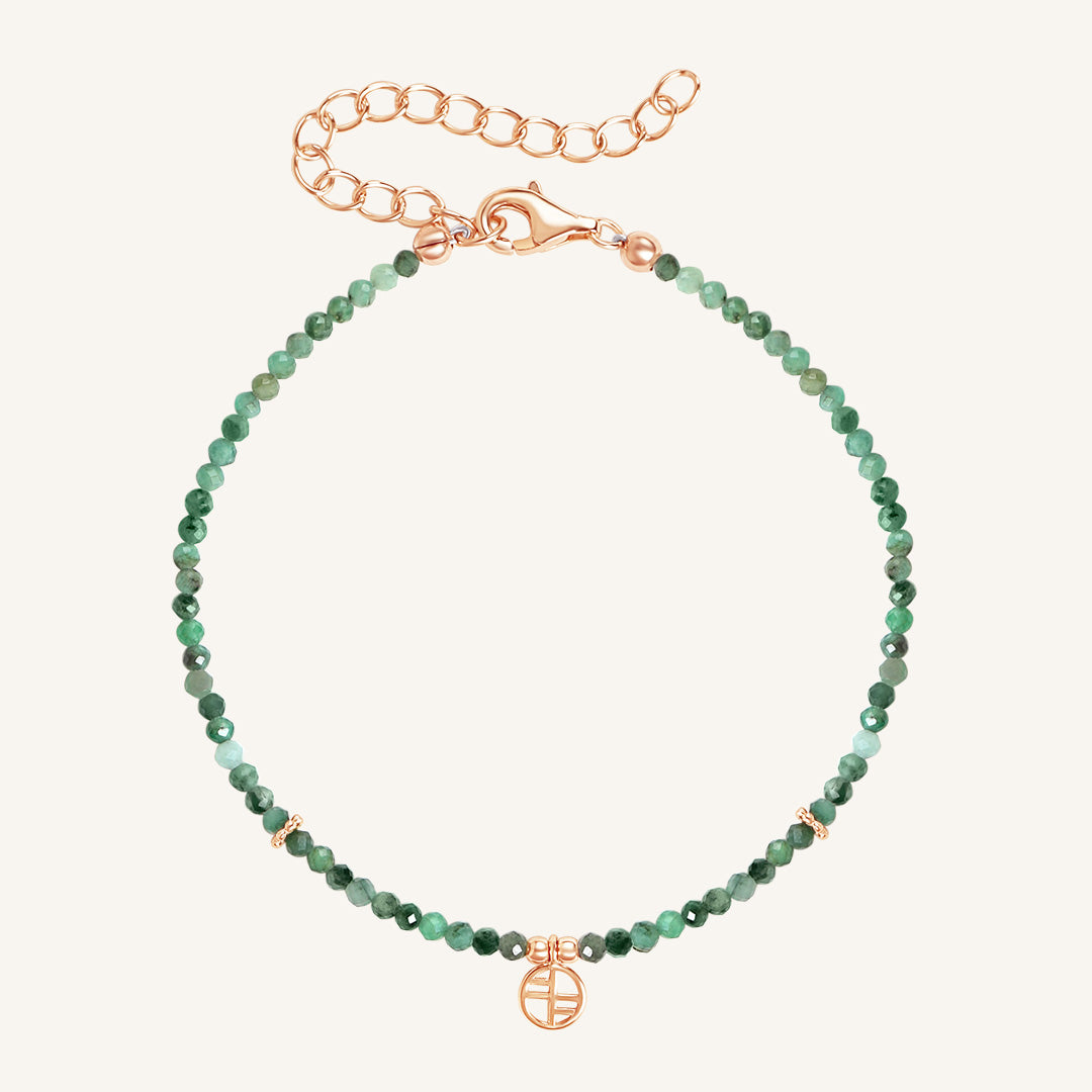 A beaded bracelet with green gemstones and a rose-tone clasp and charm.