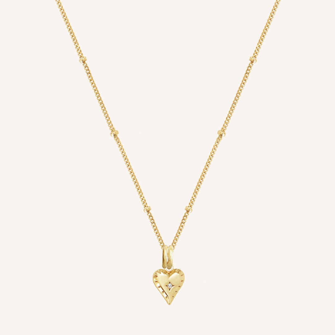 A gold-tone heart charm necklace with a fine chain, displayed against a white background.