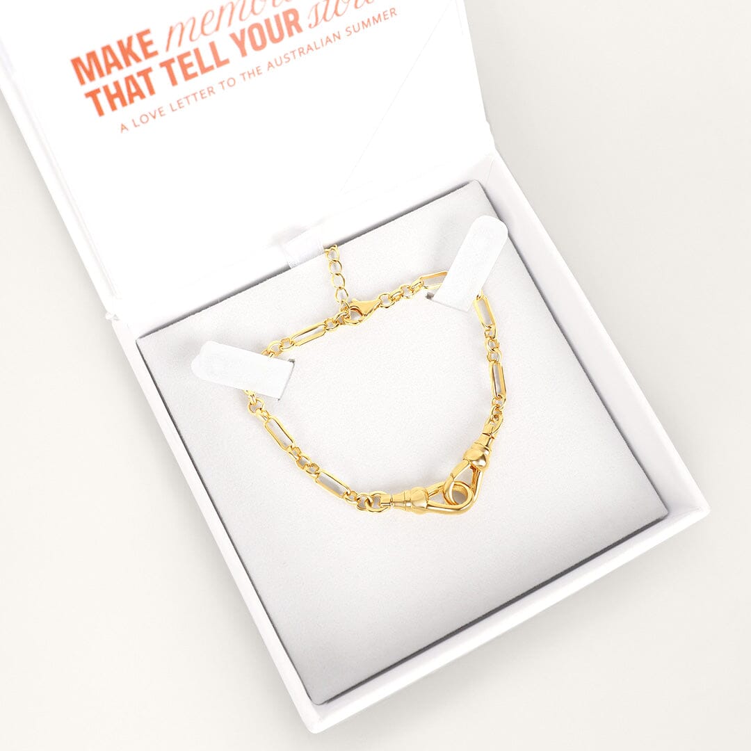 Gold chain bracelet in a white box with a card on a light gray background