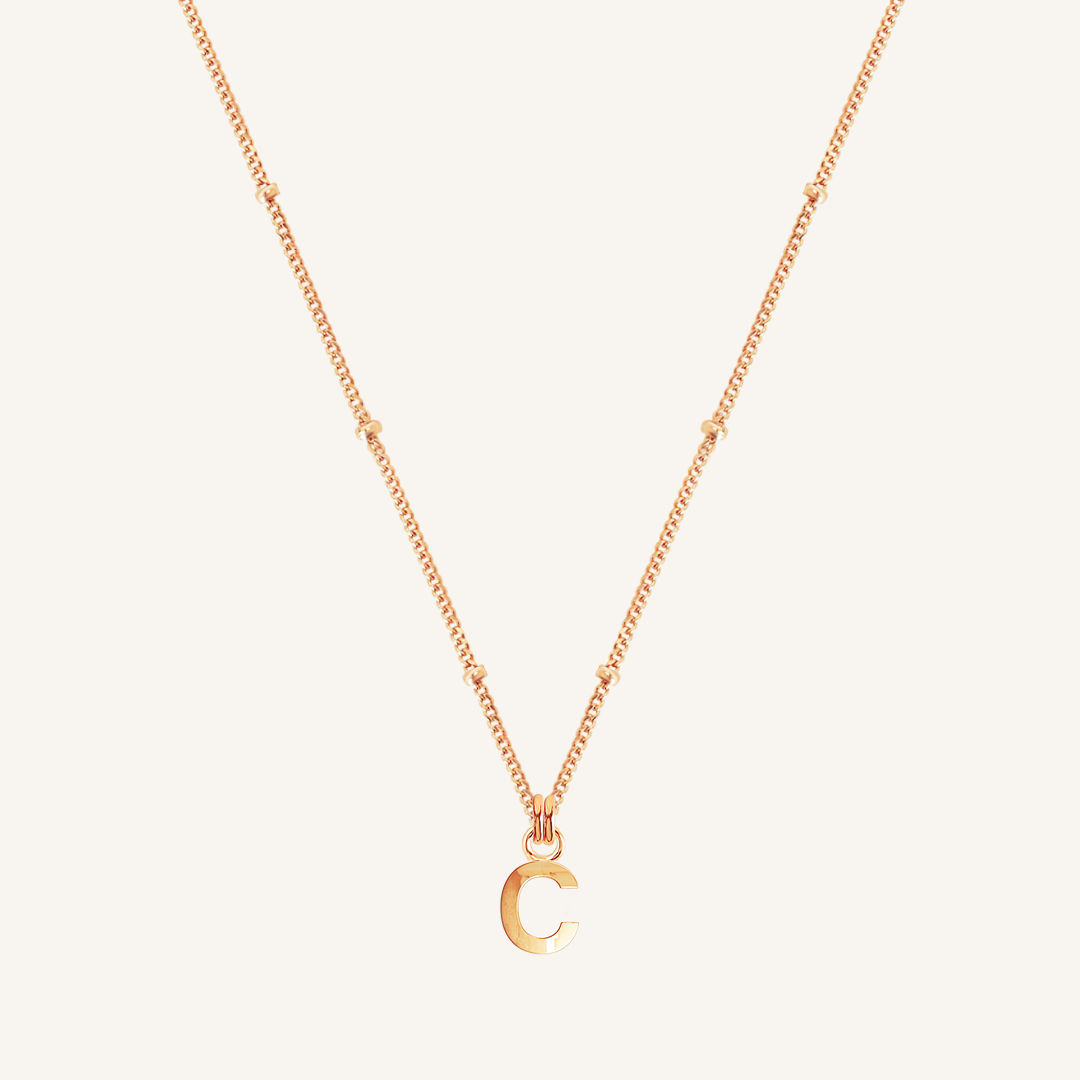 Rose gold necklace with a 'C' pendant on a light beige background