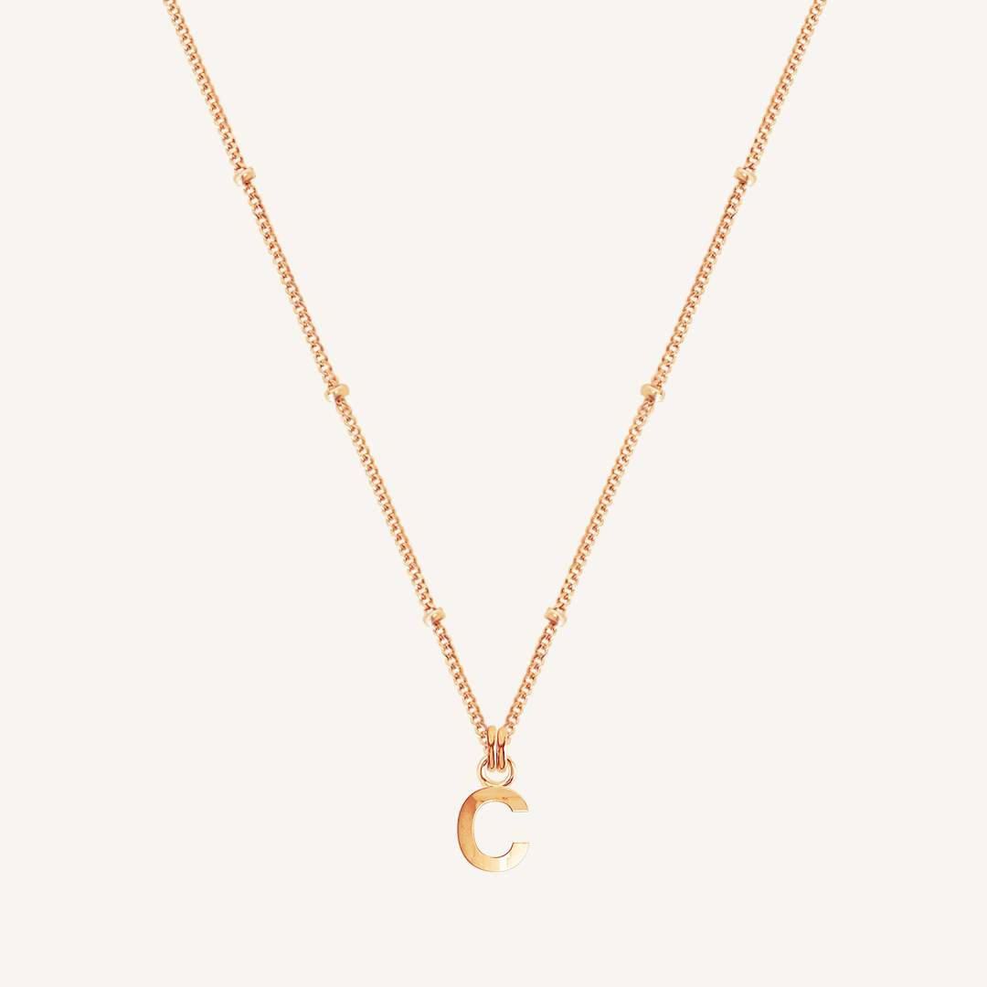Rose gold necklace with a 'C' pendant on a light beige background