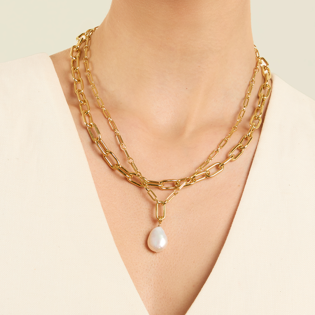A medium sized pearl charm with gold findings, attached to link chain, on models neck