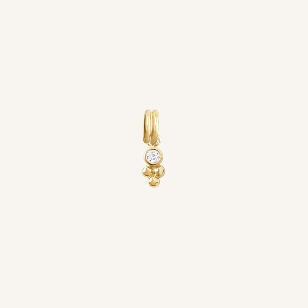 A small gold charm featuring a cubic zirconia and a floral design.