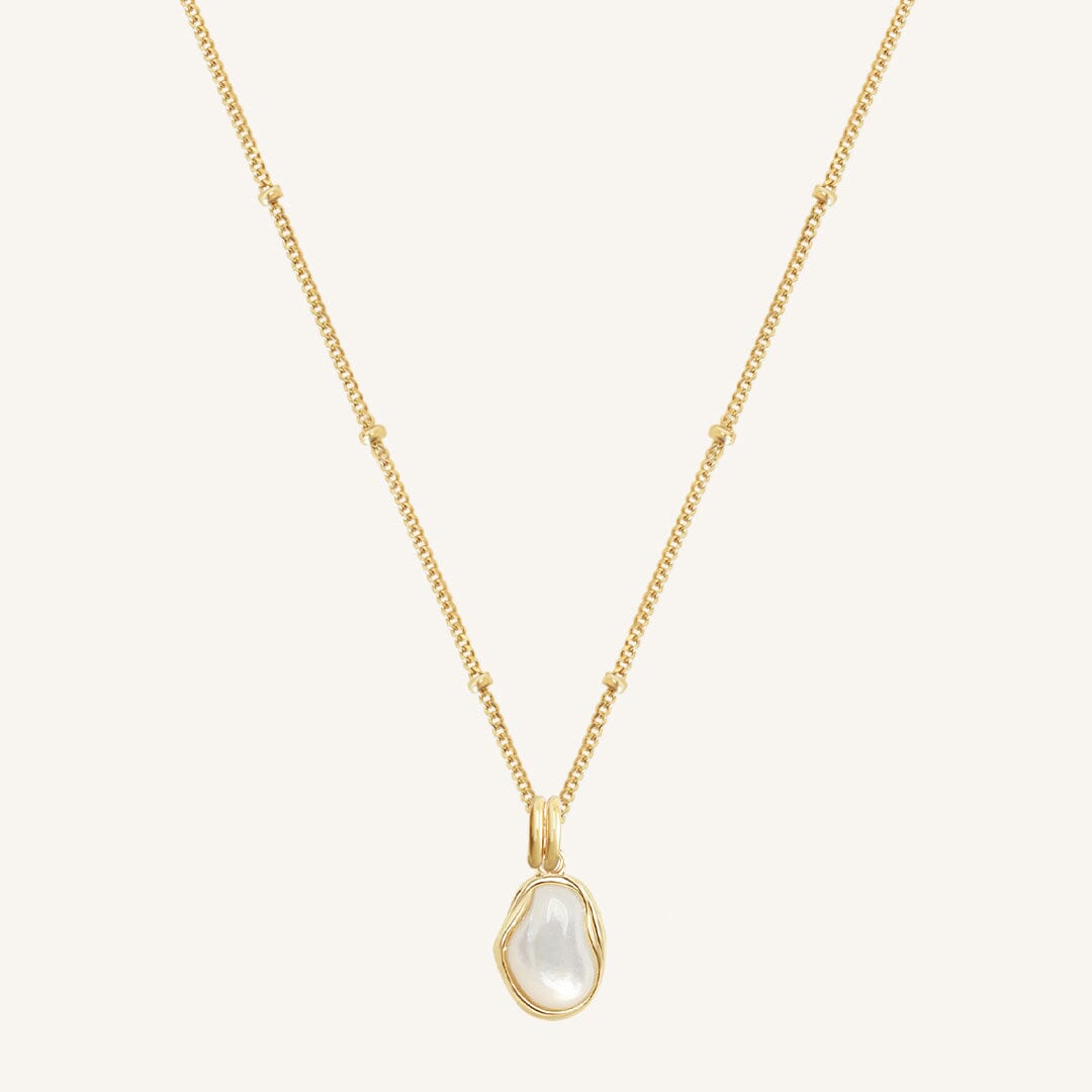 Gold necklace with a teardrop-shaped pearl pendant on a light beige background