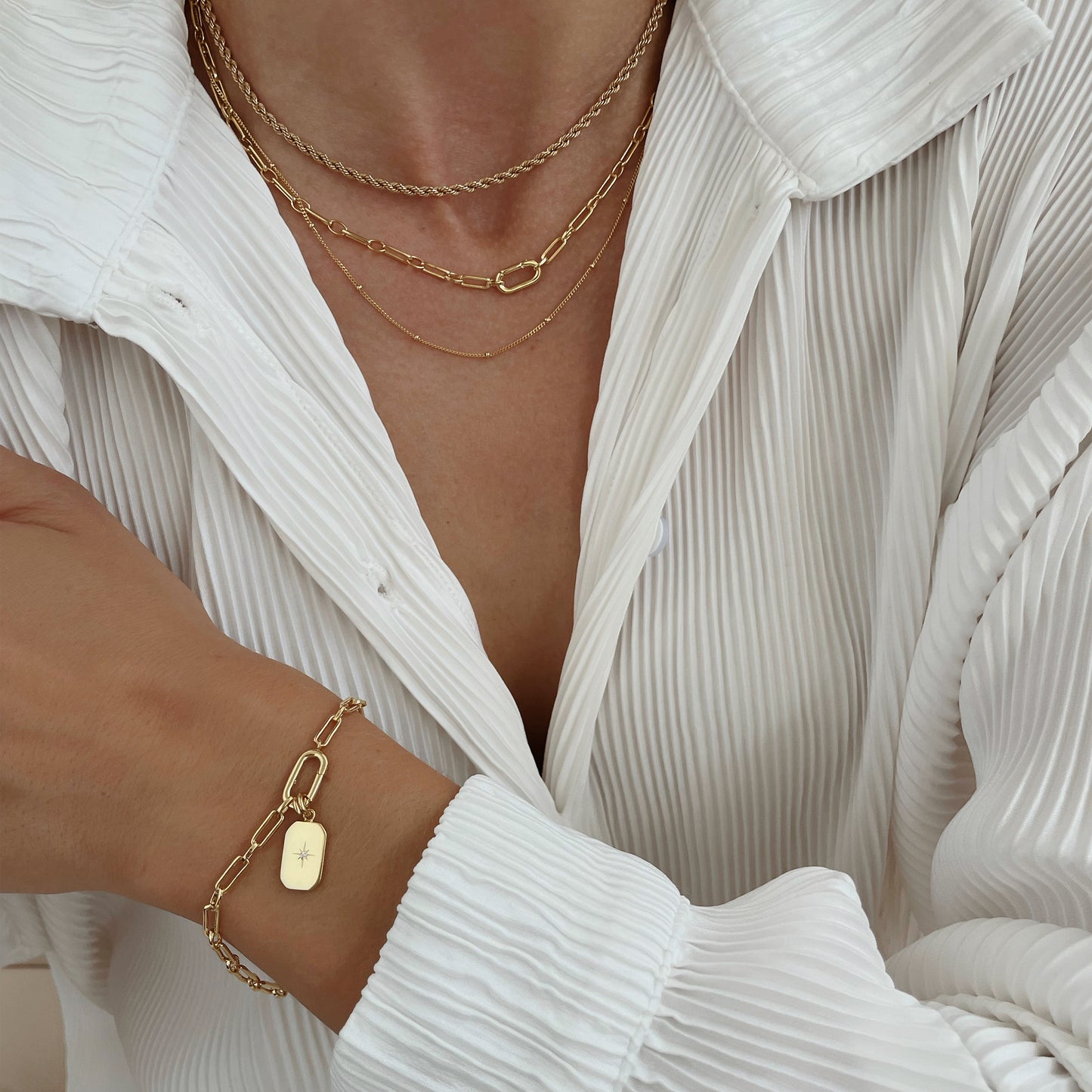 A gold-toned link bracelet with charm attached to it, worn on models wrist