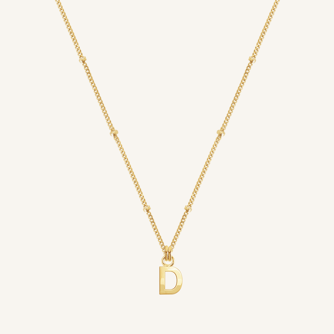 Gold necklace with a 'D' pendant on a light beige background