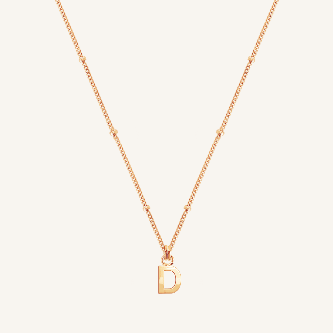 Gold necklace with a 'D' pendant on a light beige background