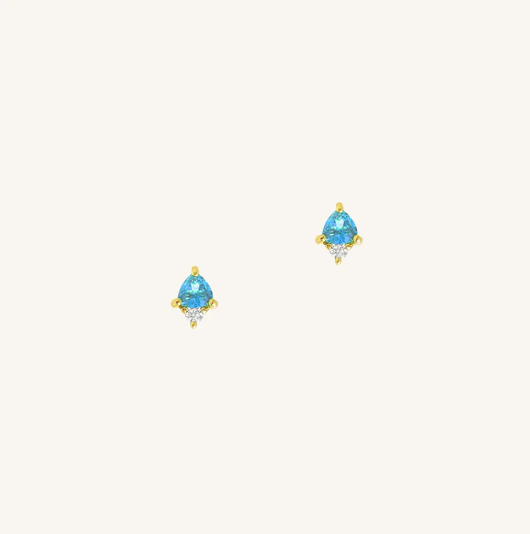 A gold pair of stud earrings featuring a blue cubic zirconia, representing December.