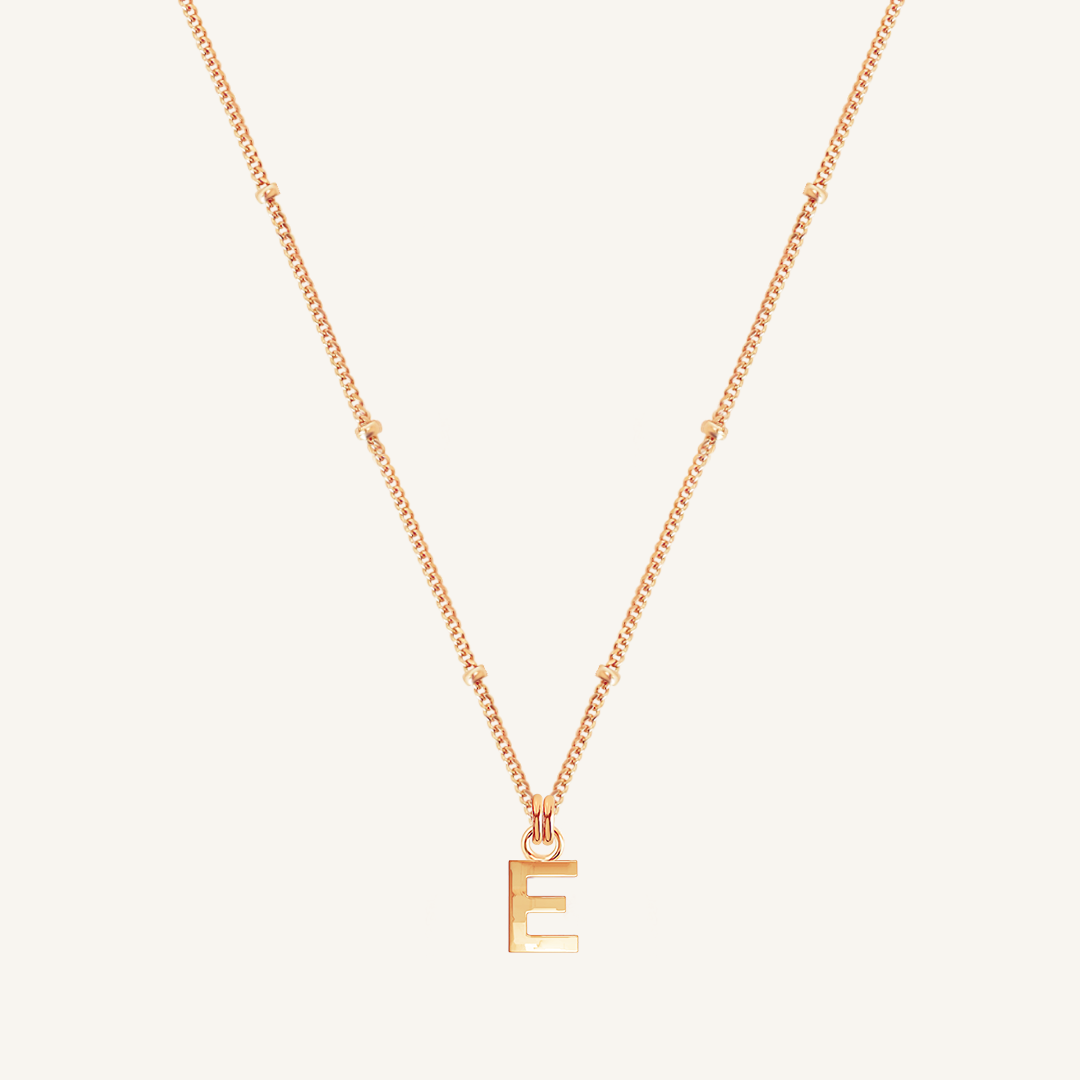 Rose gold necklace with a 'E' pendant on a light beige background