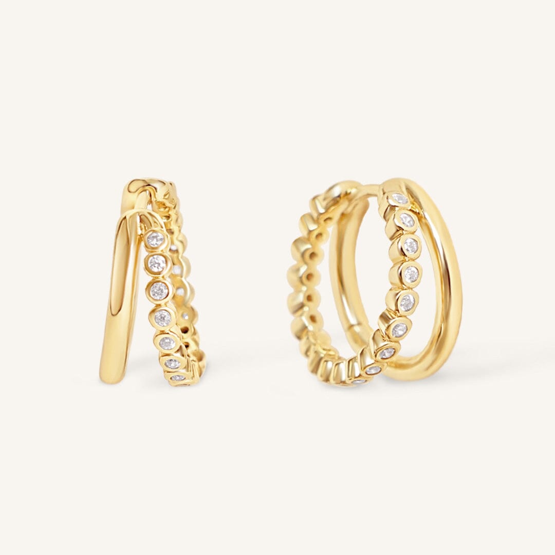 Gold double hoop earrings with embedded stones on a light beige background