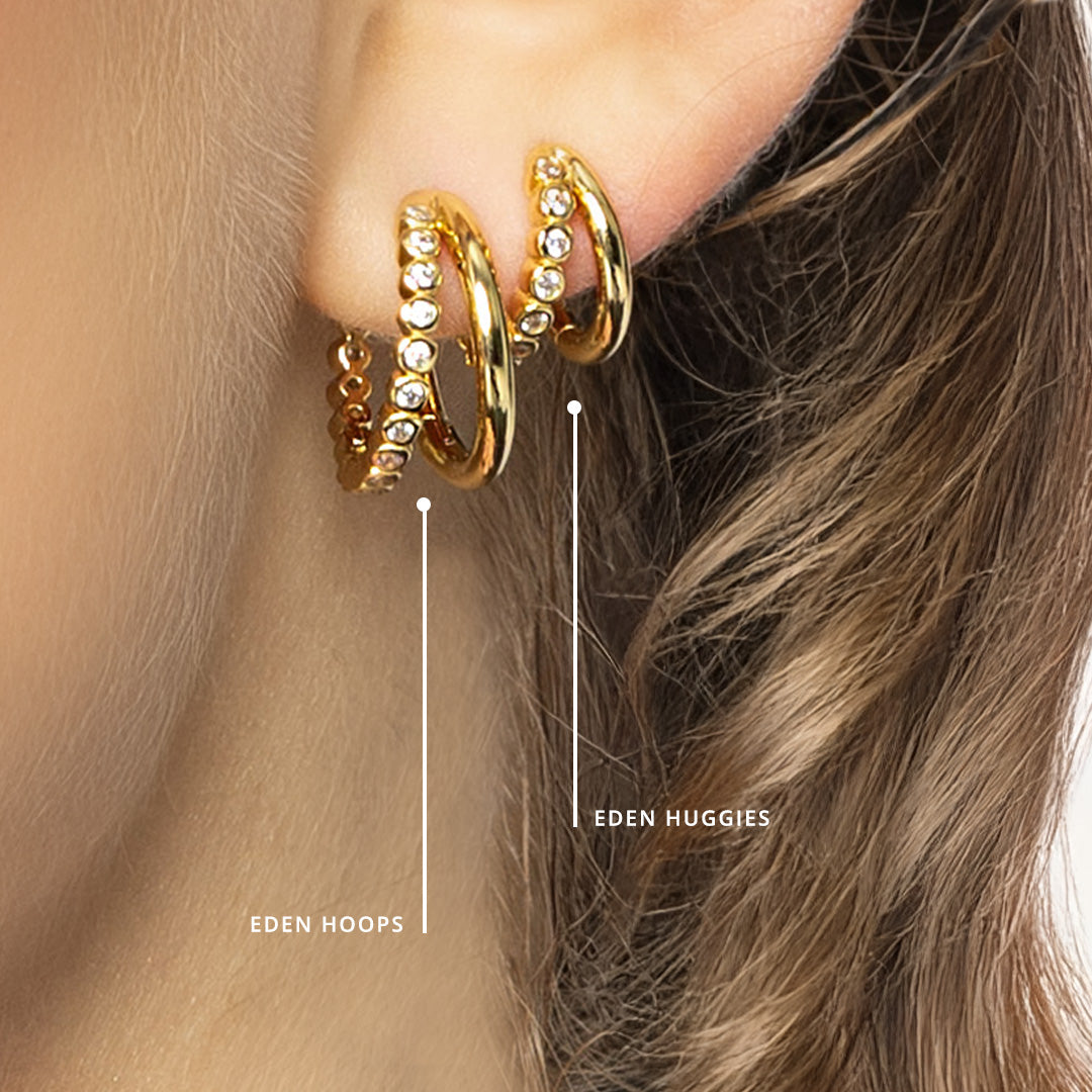 Gold hoop earrings worn by a person with brown hair, labeled 'Eden Hoops' and 'Eden Huggies'.