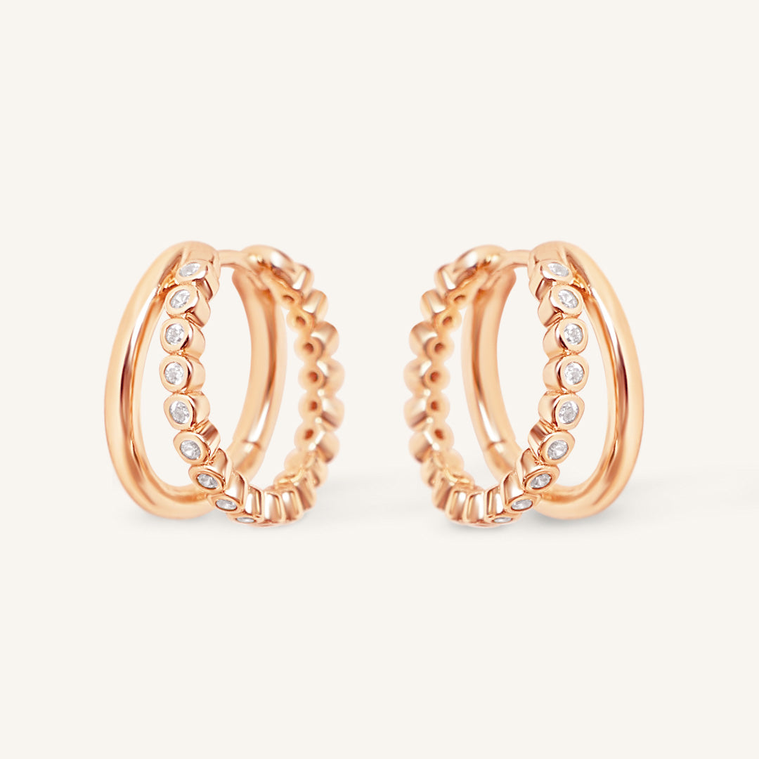 Pair of rose gold hoop earrings with cubic zirconias on a light beige background