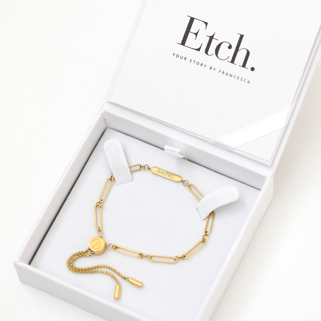 A gold chain bracelet with an adjustable fastening design and an engraveable panel in white box
