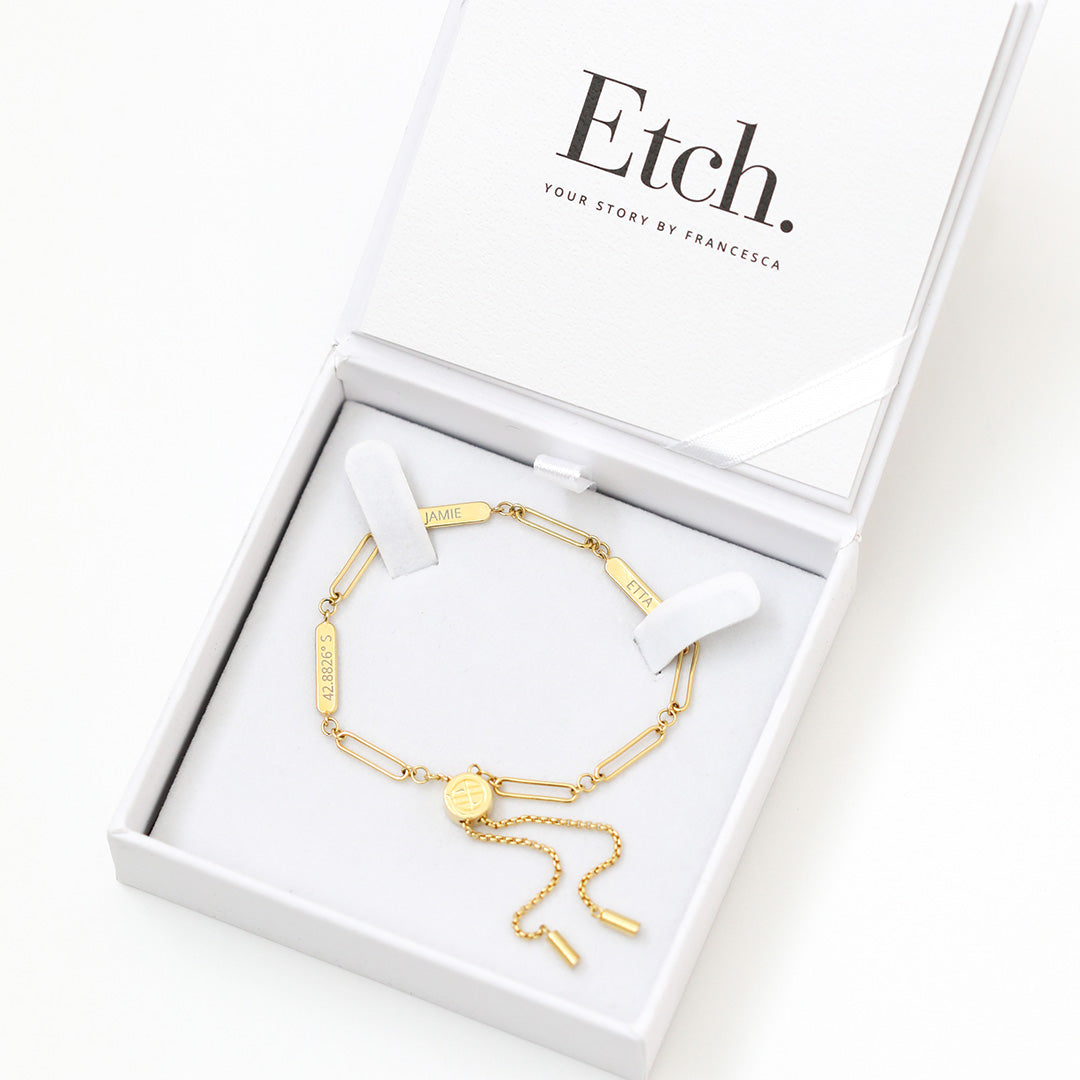 A gold Etch chain bracelet with three panels for engraving, featuring an adjustable fastening mechanism, displayed in a white box