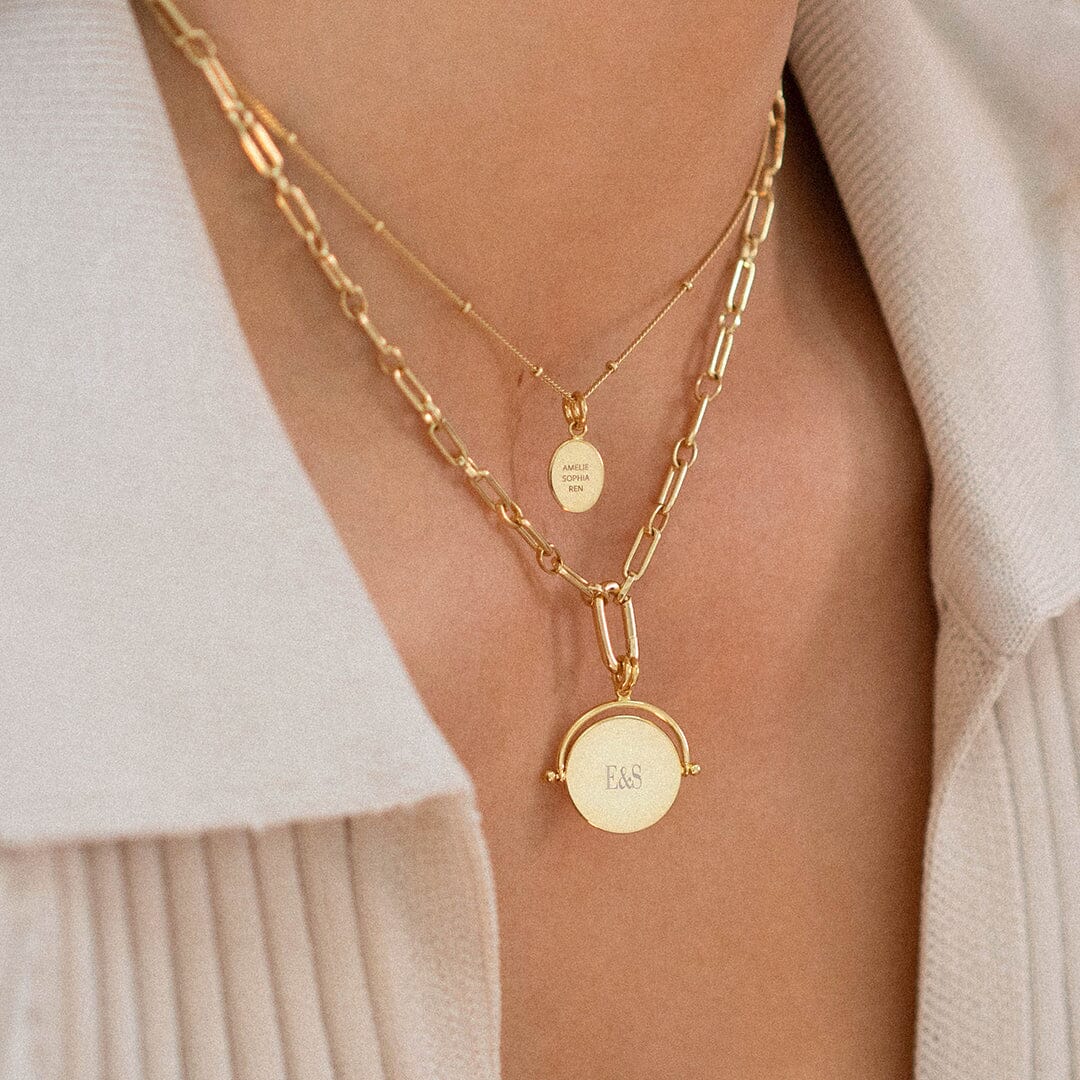 A gold-coloured, engraved pendant with, featuring a spinning mechanism, attached do a gold chain, on neck, layered with gold chains