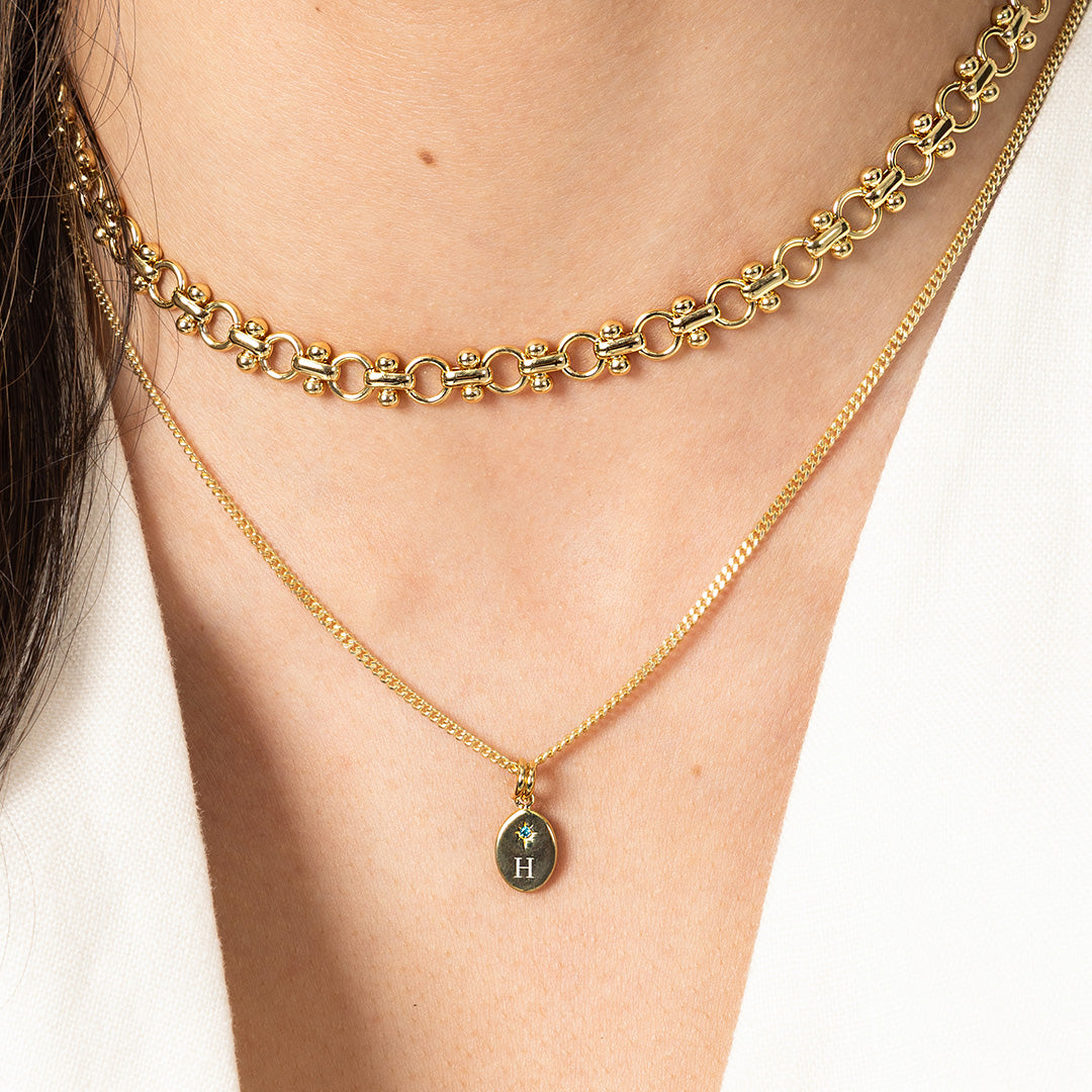 Two gold necklaces on a person's neck with one featuring a pendant.