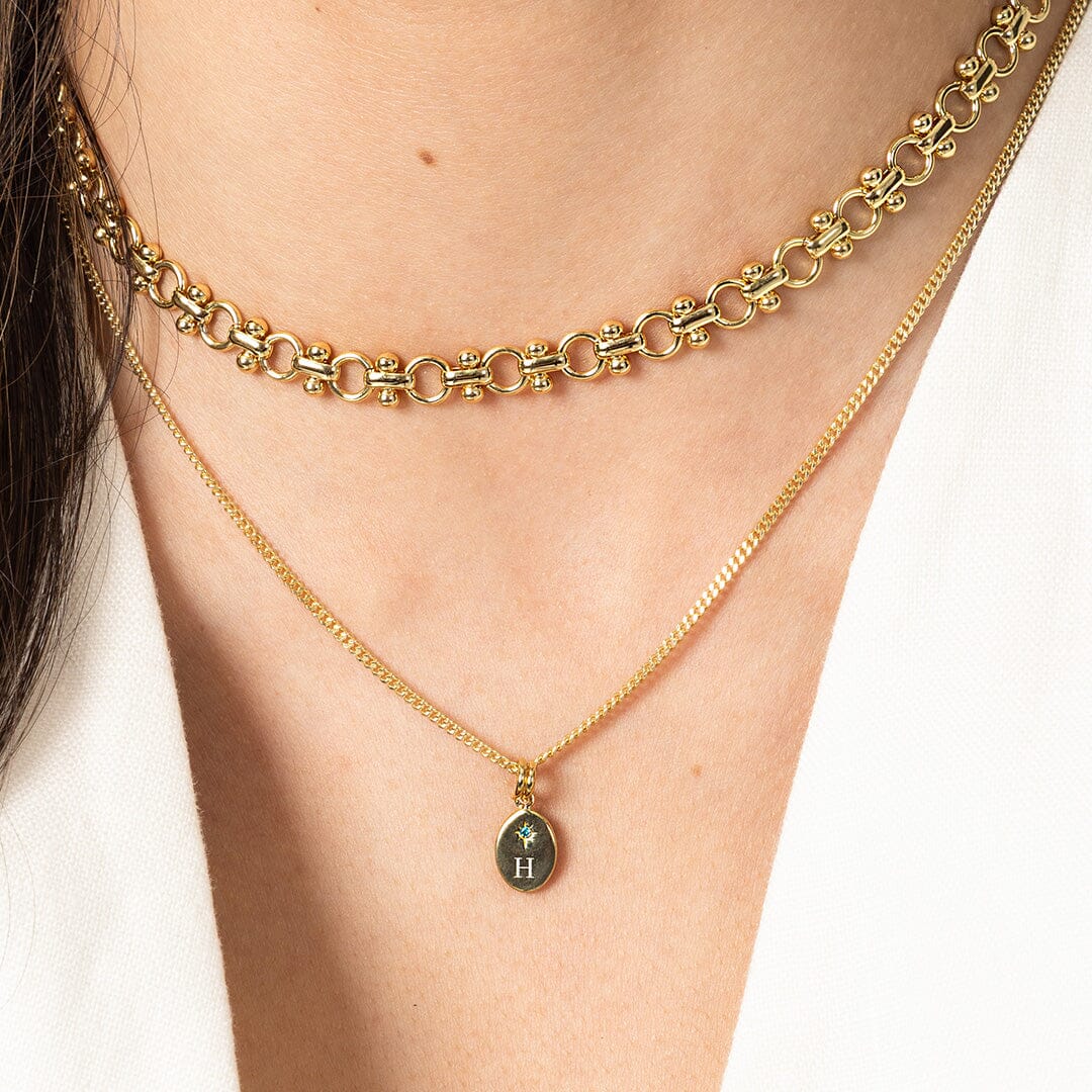Two gold necklaces on a person's neck with one featuring a pendant.